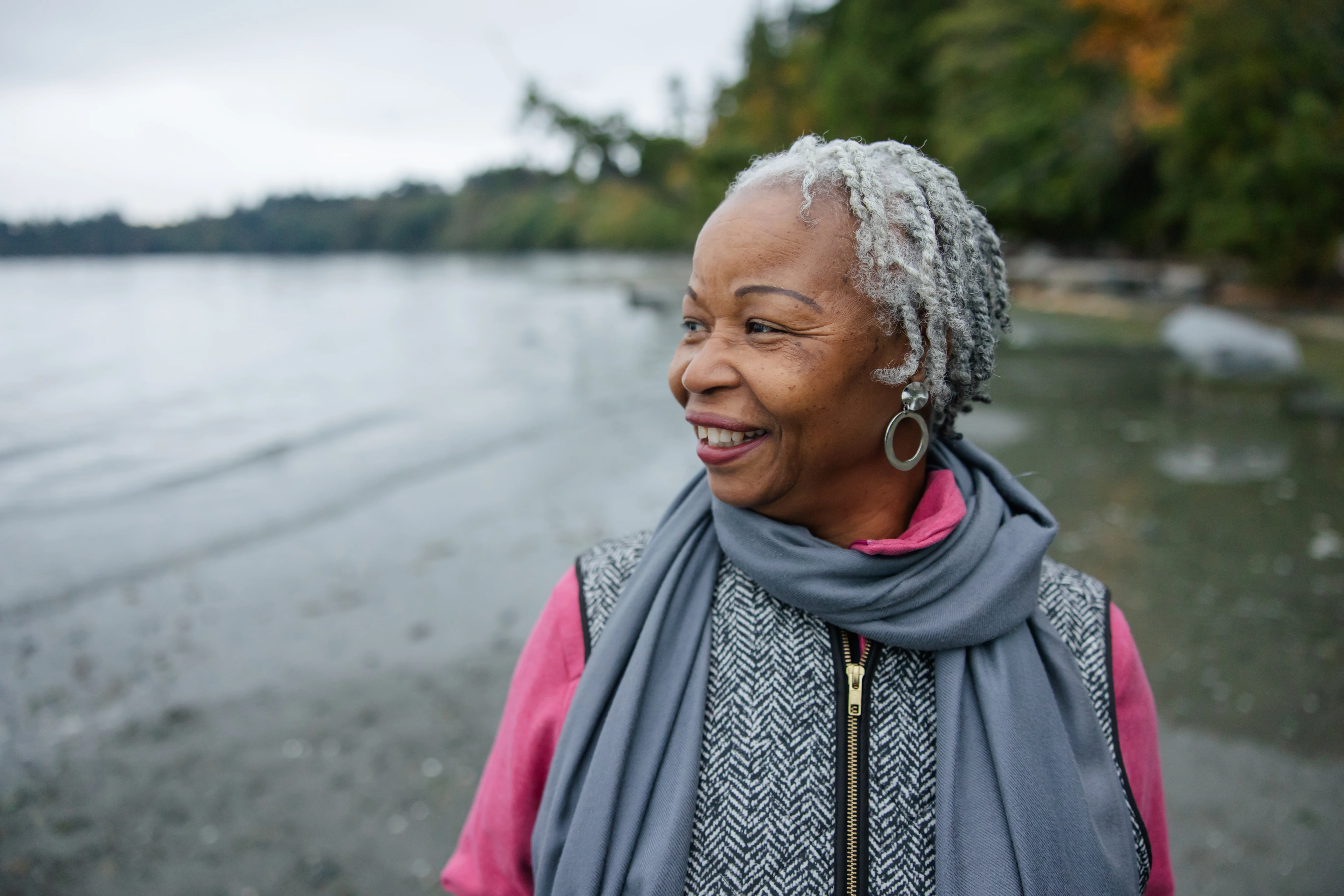 Following a successful stoma surgery, a smiling elderly woman stands by a lake as she returns to her normal life.